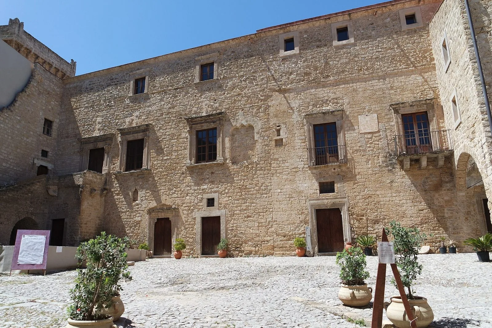 Facciata in pietra del cortile interno del Castello La Grua-Talamanca di Carini con finestre rinascimentali e vasi di piante